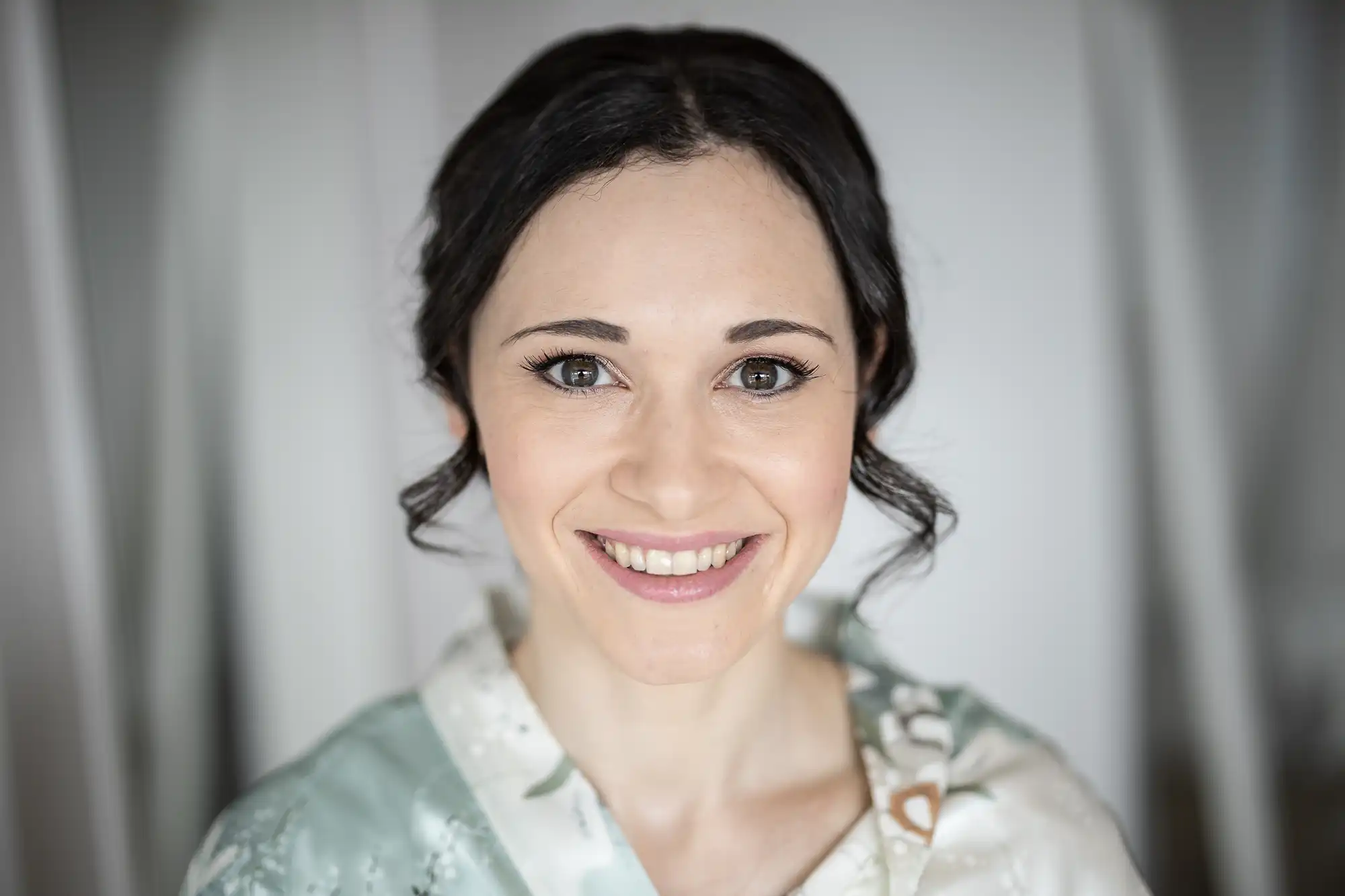 A woman with dark hair in an updo smiles, wearing a patterned wrap.