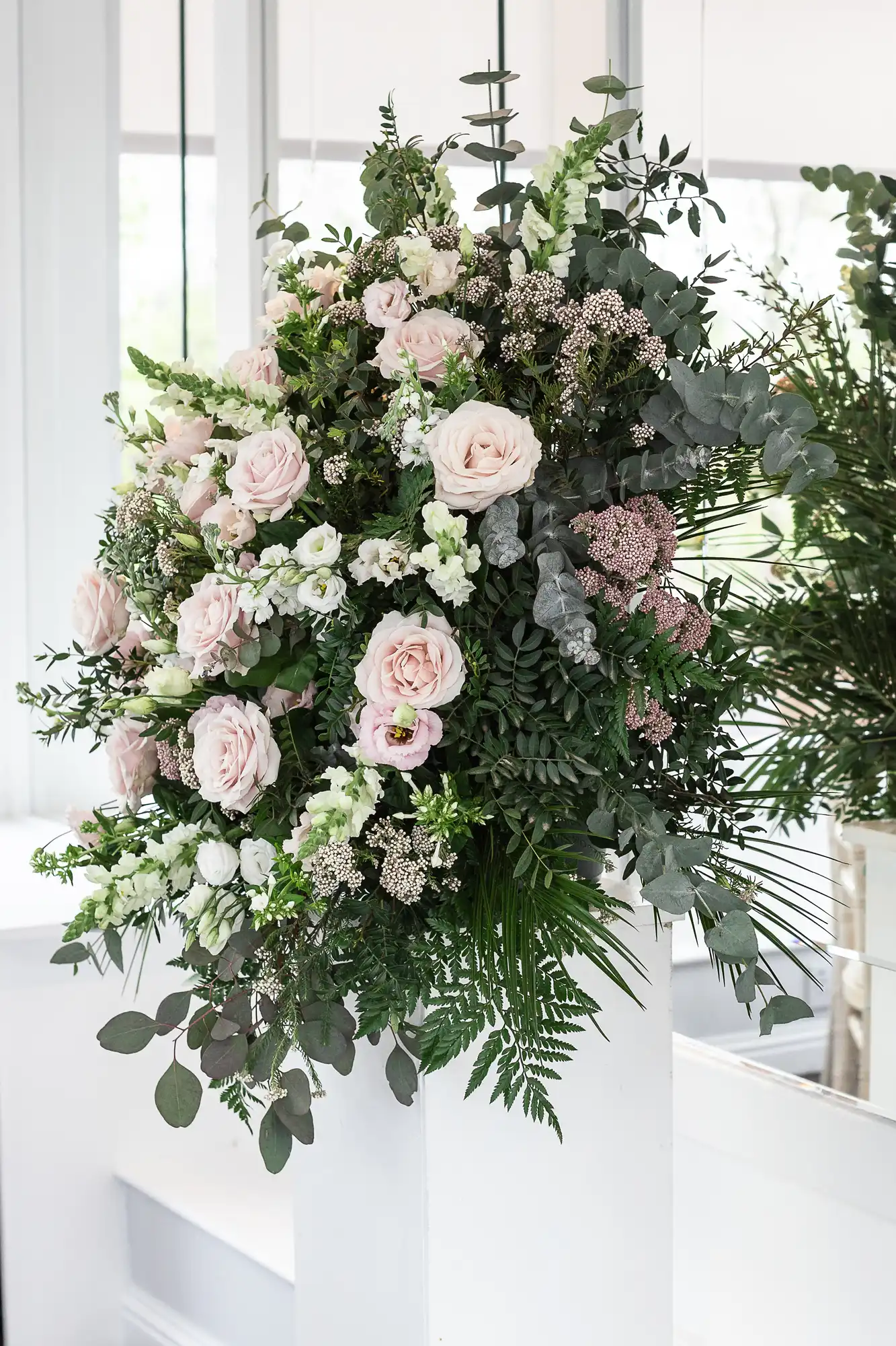 Floral arrangement with pink roses, white flowers, and greenery against a white wall with mirrors.