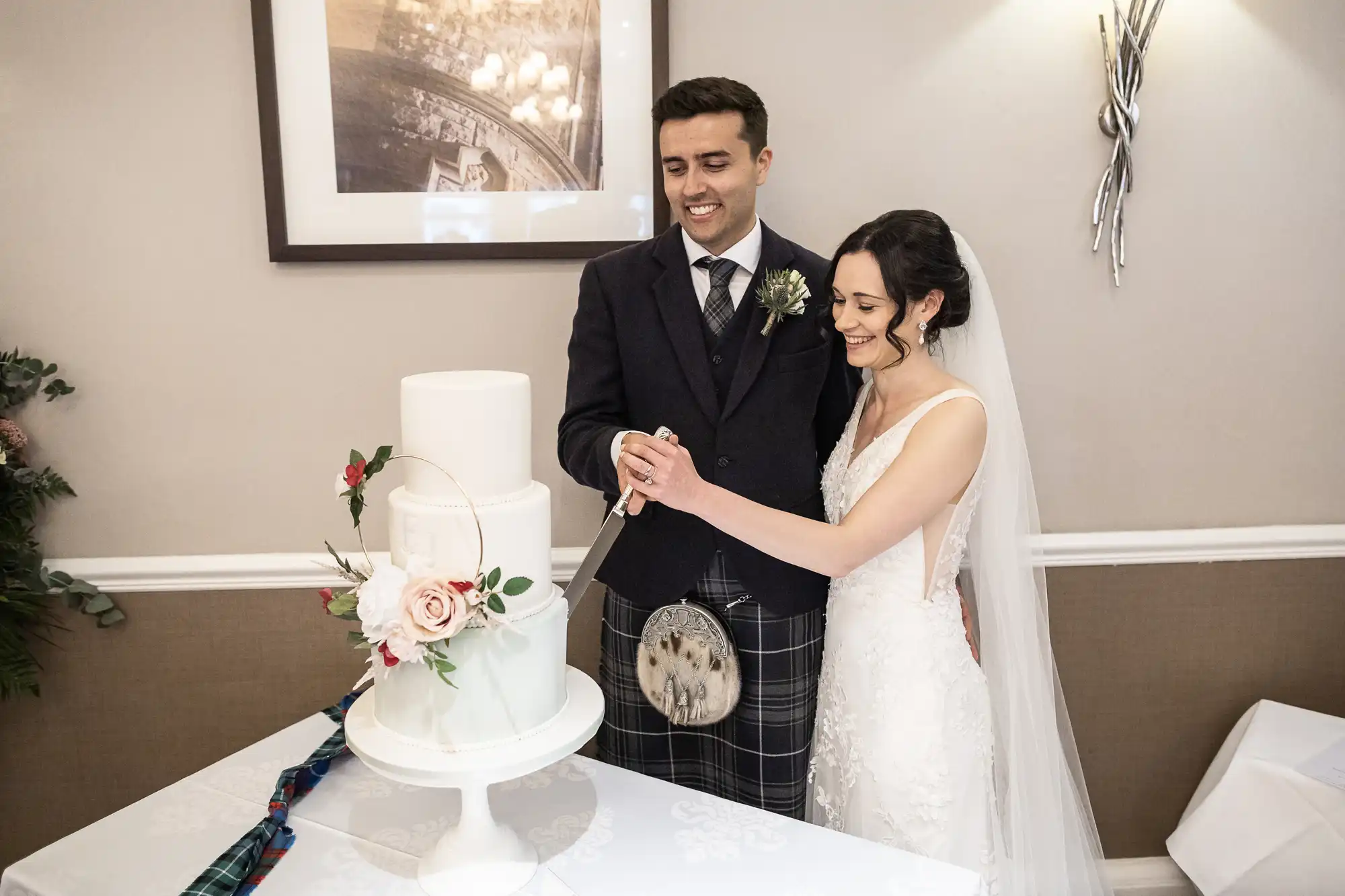 Bride and groom smiling as they cut a tiered wedding cake decorated with flowers.