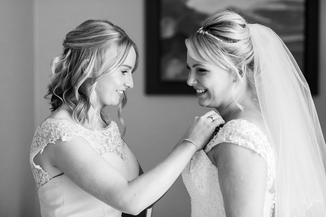 bridesmaid helps bride put on necklace