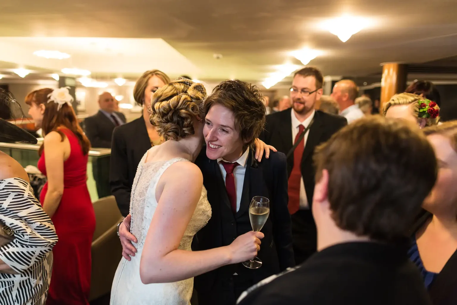 A bride and groom embracing and smiling at each other amidst guests at a wedding reception.