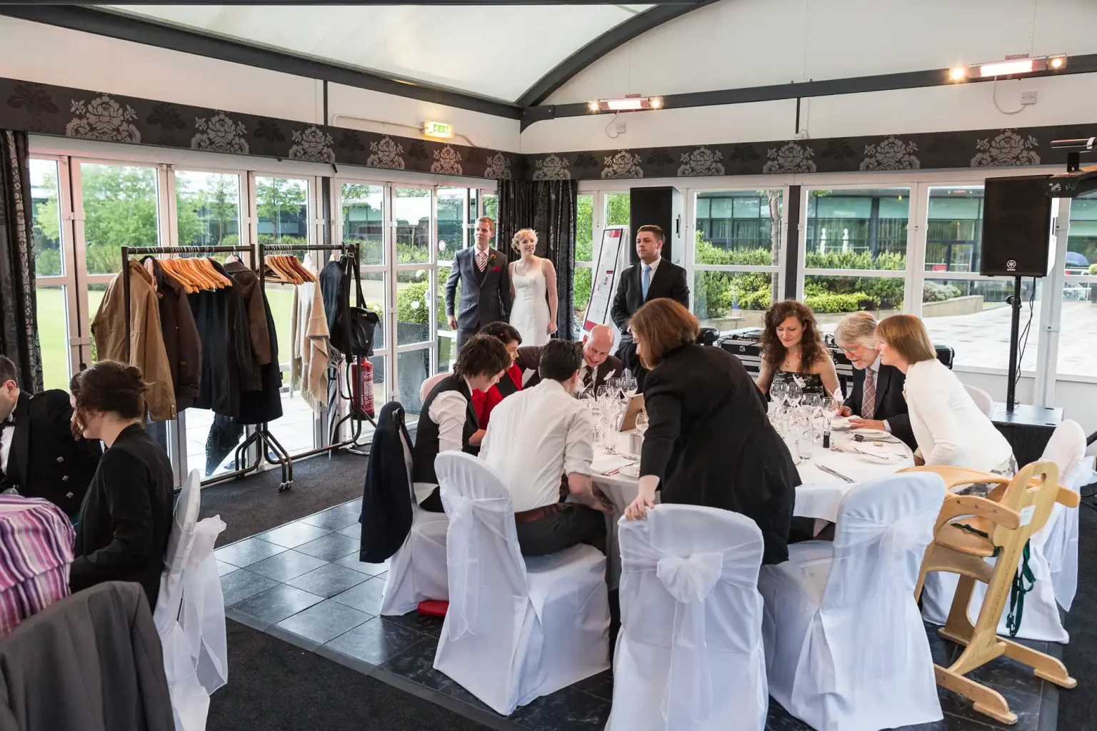 A bride and groom entering a wedding reception hall, where guests are seated at tables with white chairs and tablecloths.