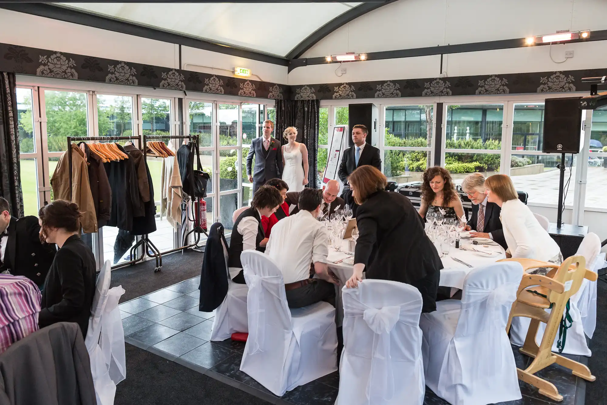 A bride and groom entering a wedding reception hall, where guests are seated at tables with white chairs and tablecloths.