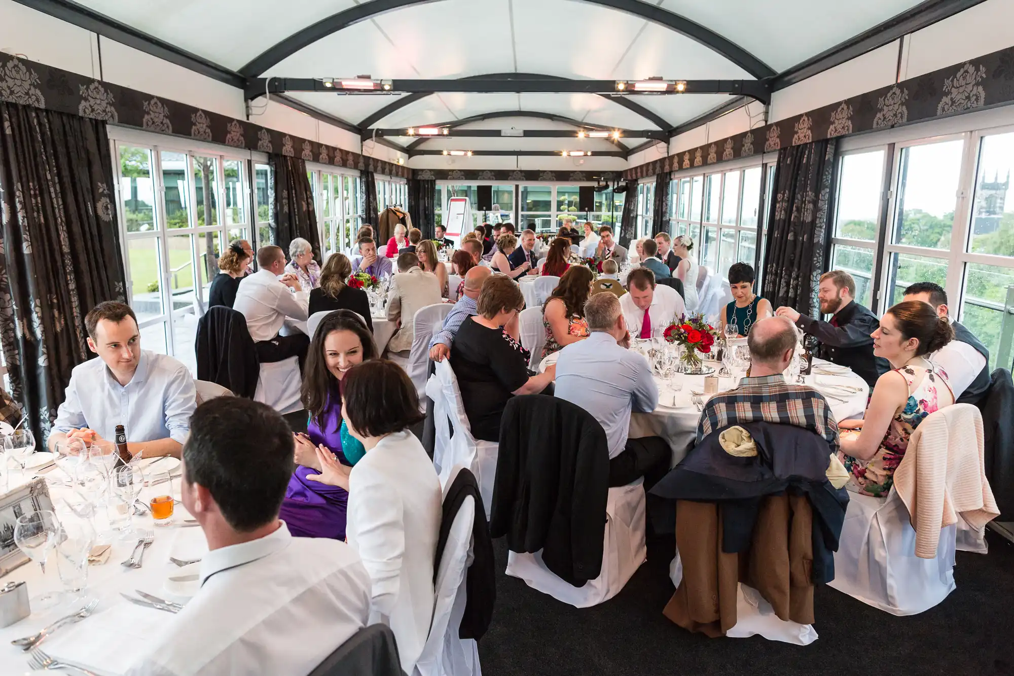 Diverse group of people dining in an elegant, elongated restaurant car of a train with large windows and patterned decor.