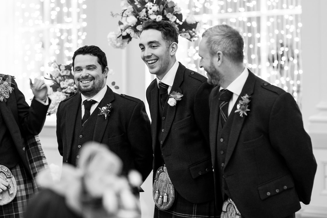 groomsmen laughing as they wait for the arrival of the bride in the Kings Hall