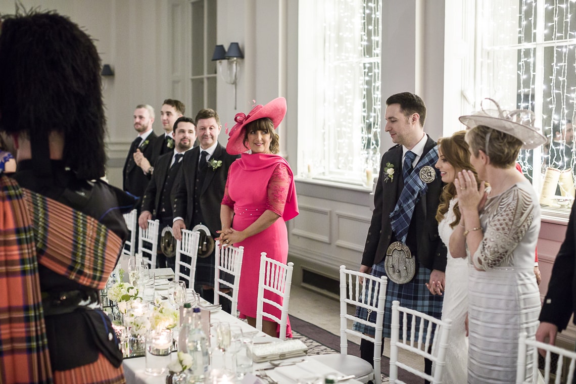 bride and groom are escorted by the piper to the top table