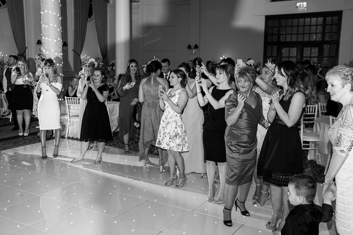 guests watching and taking photos of the newlyweds cutting the cake in the King's Hall