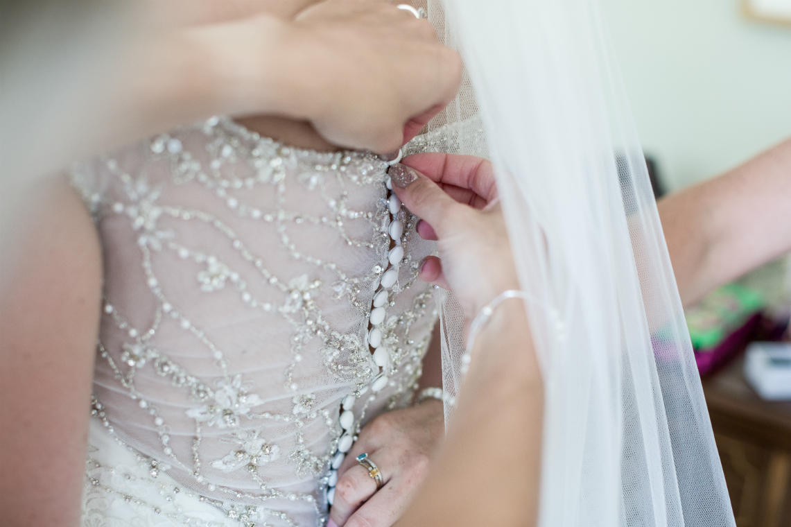 bridesmaid buttoning up the back of the bride's wedding dress