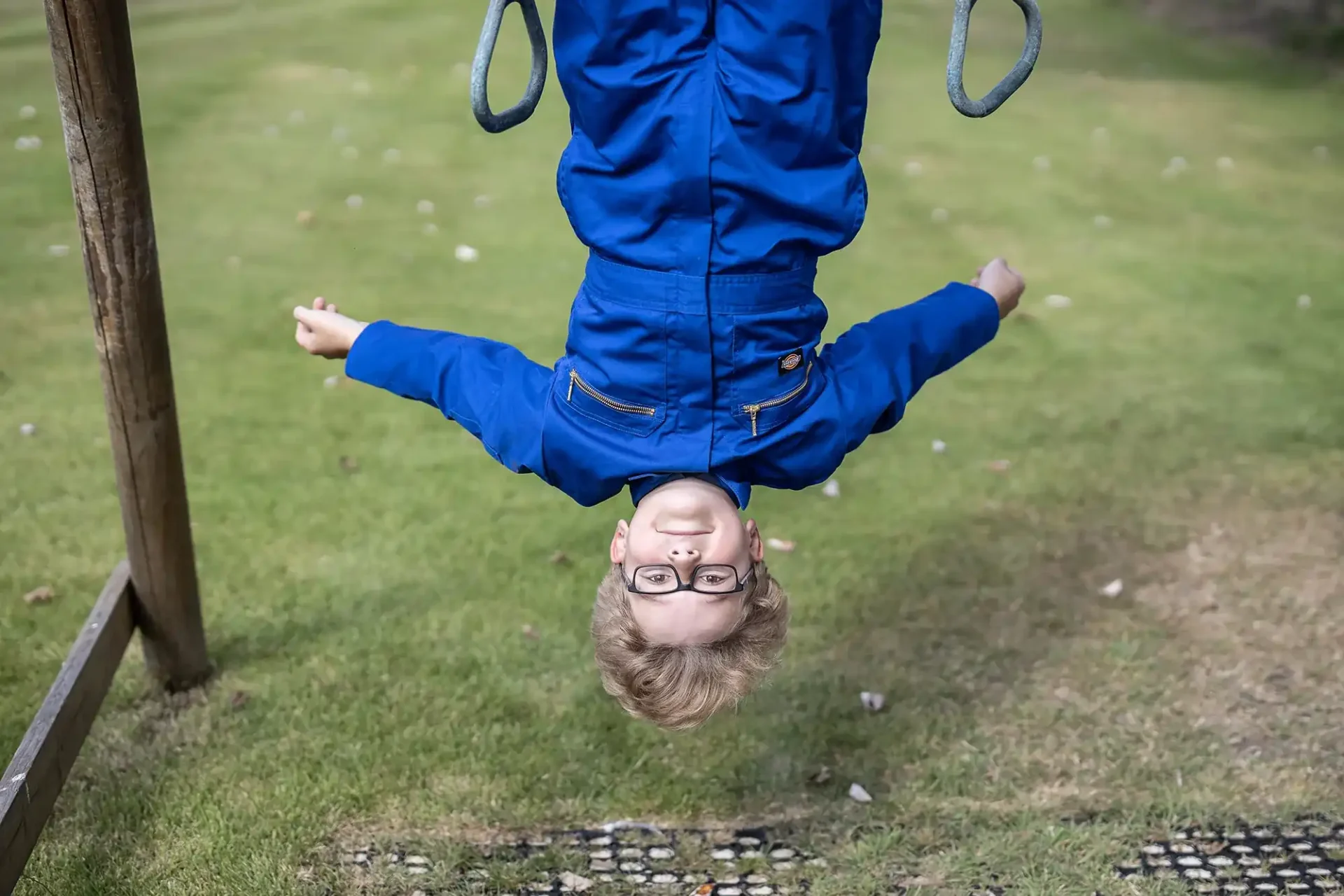 young boy dangles upside down from a slide