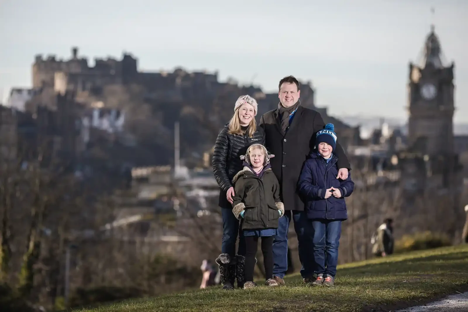 Four pose outdoors with a historic castle and clock tower in the background.