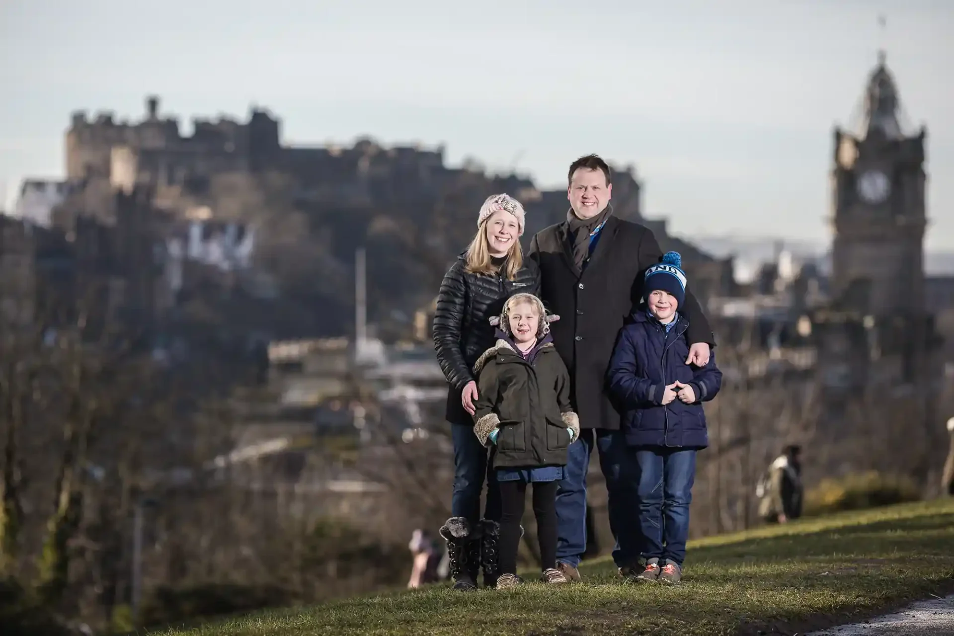 Four pose outdoors with a historic castle and clock tower in the background.