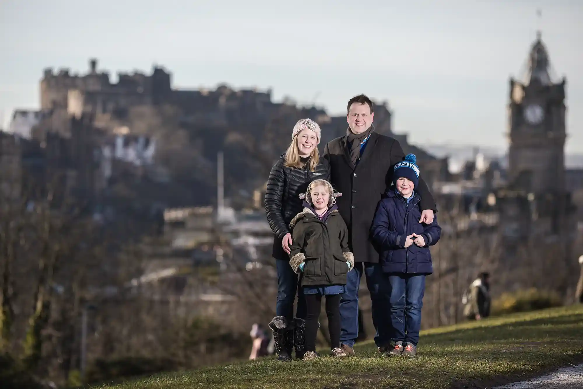 Four pose outdoors with a historic castle and clock tower in the background.