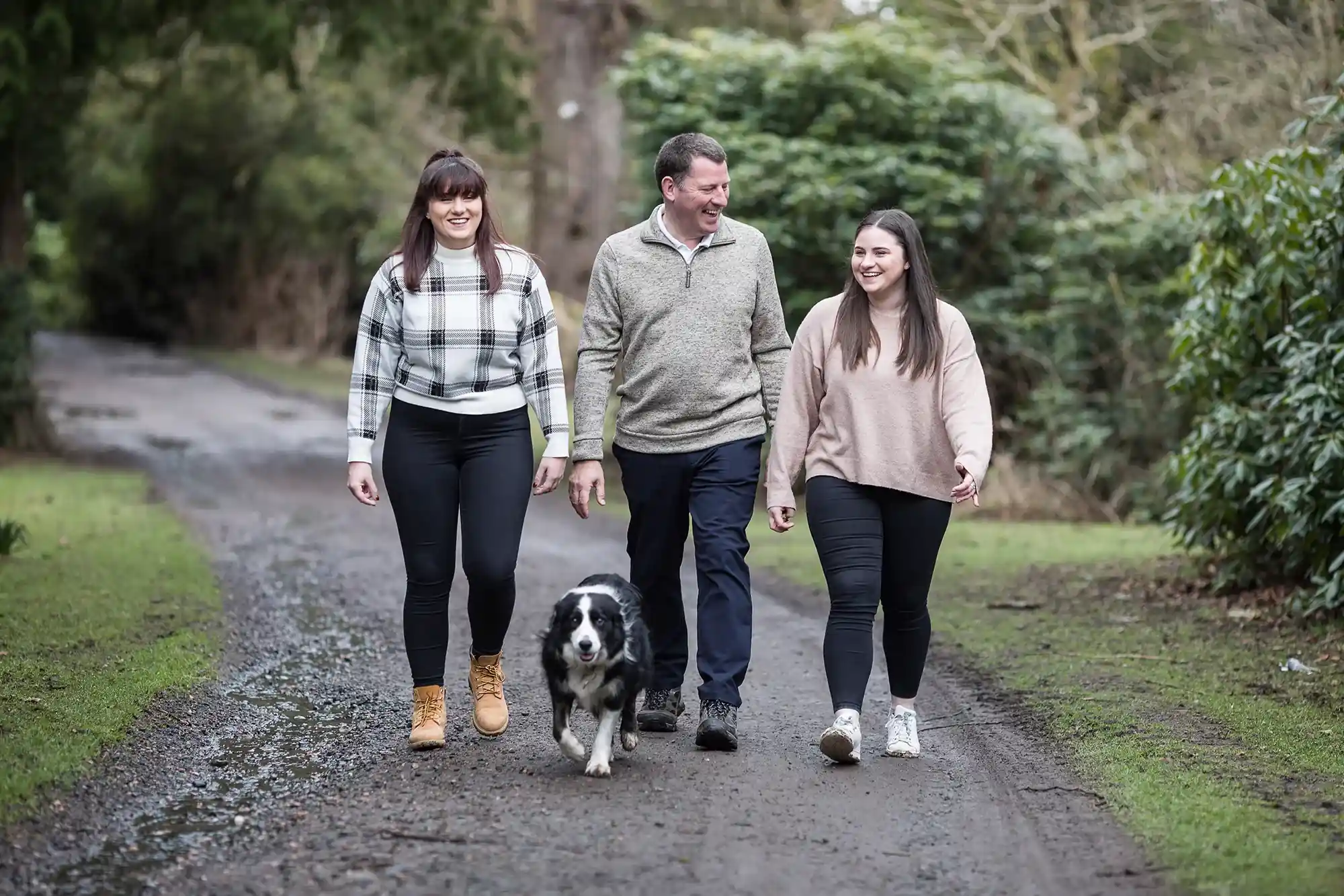 Three people and a dog walking on a path in a wooded area. The two women are on either side of the man in the center, with the black and white dog between them.