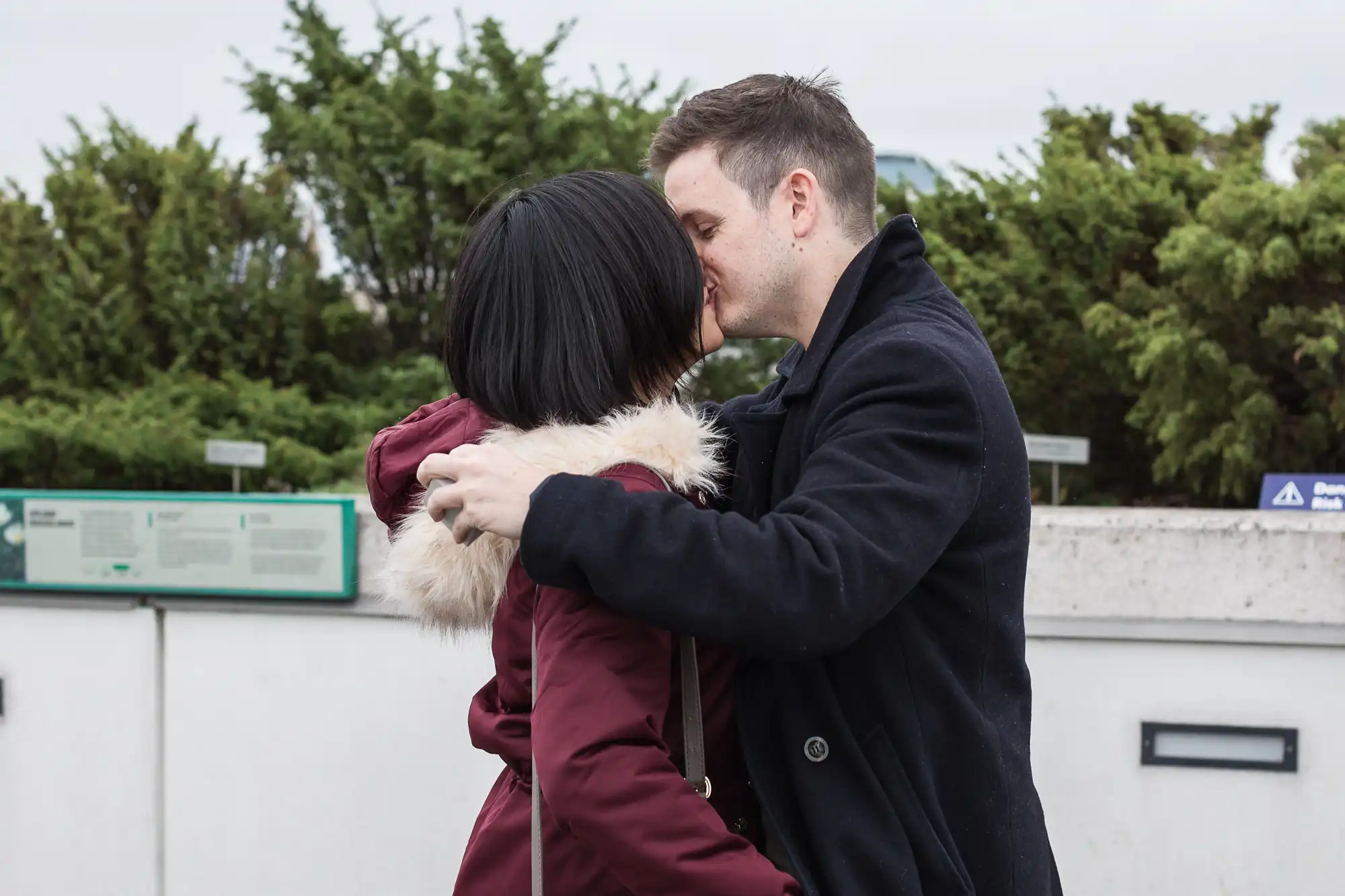 A man kissing a woman on the forehead in an affectionate embrace outdoors.