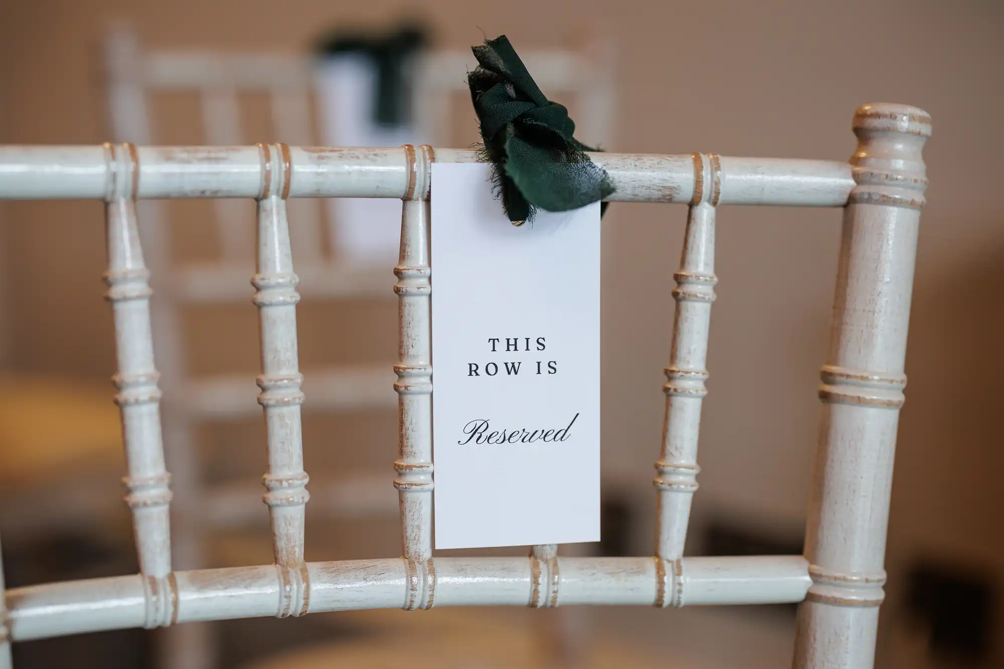A white chair with a "THIS ROW IS Reserved" sign tied with dark green ribbon.