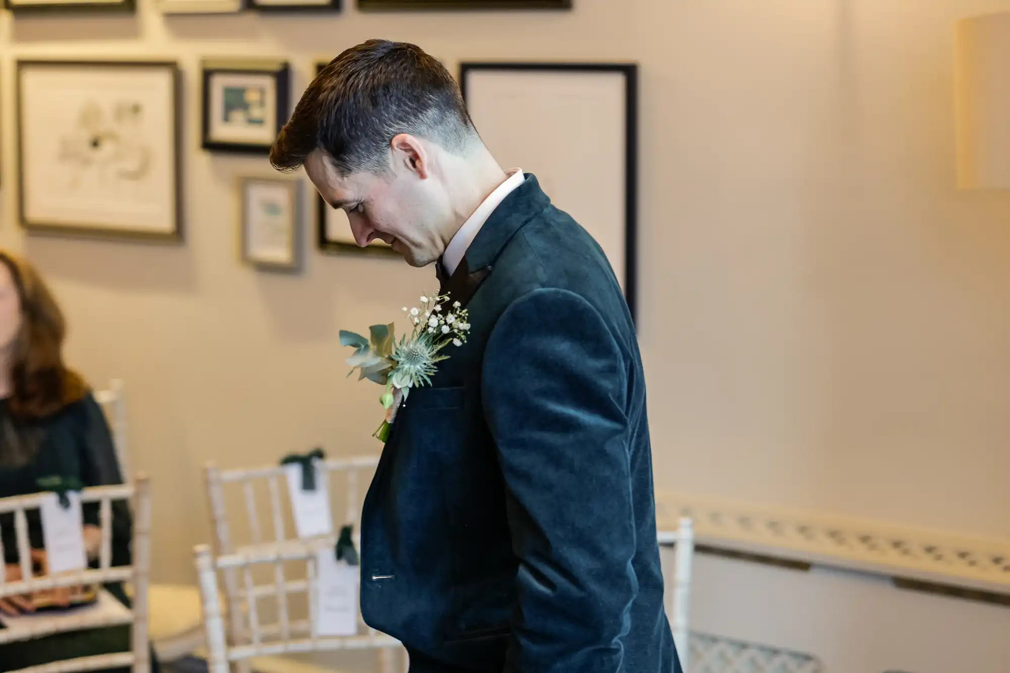 Groom in a teal velvet suit with a boutonnière of thistles and baby's breath, looking down with a slight smile.