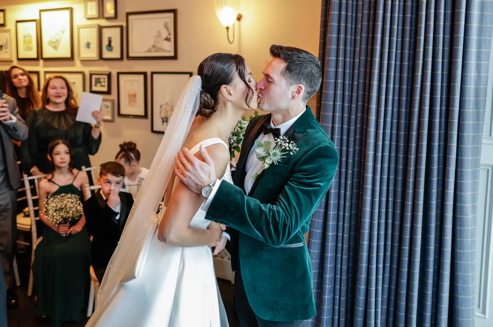 A bride and groom share a tender kiss, the bride in a white gown and veil, the groom in a striking emerald green velvet jacket.