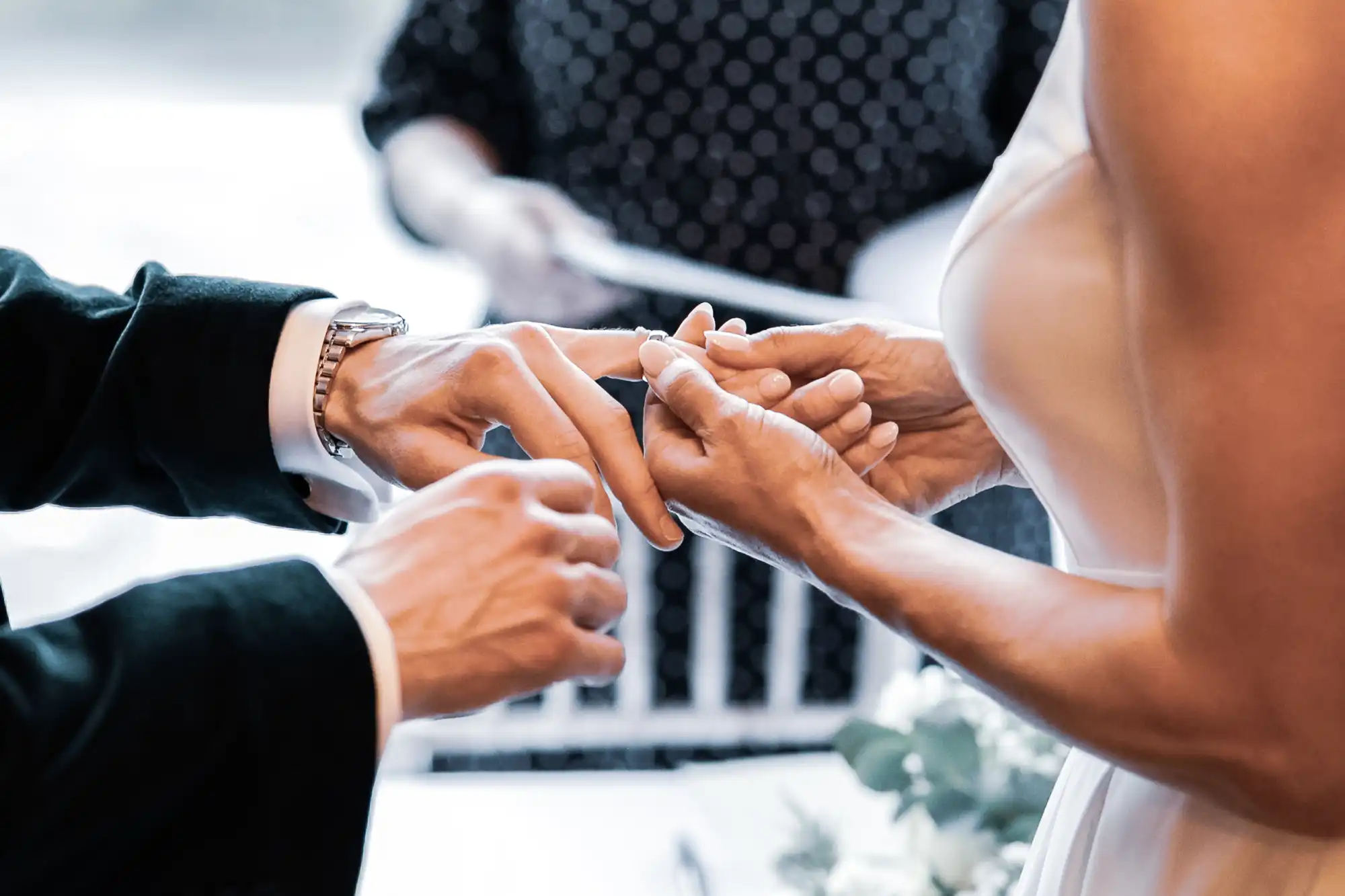 A groom in a black suit and a bride in a white dress exchange wedding rings during a ceremony.