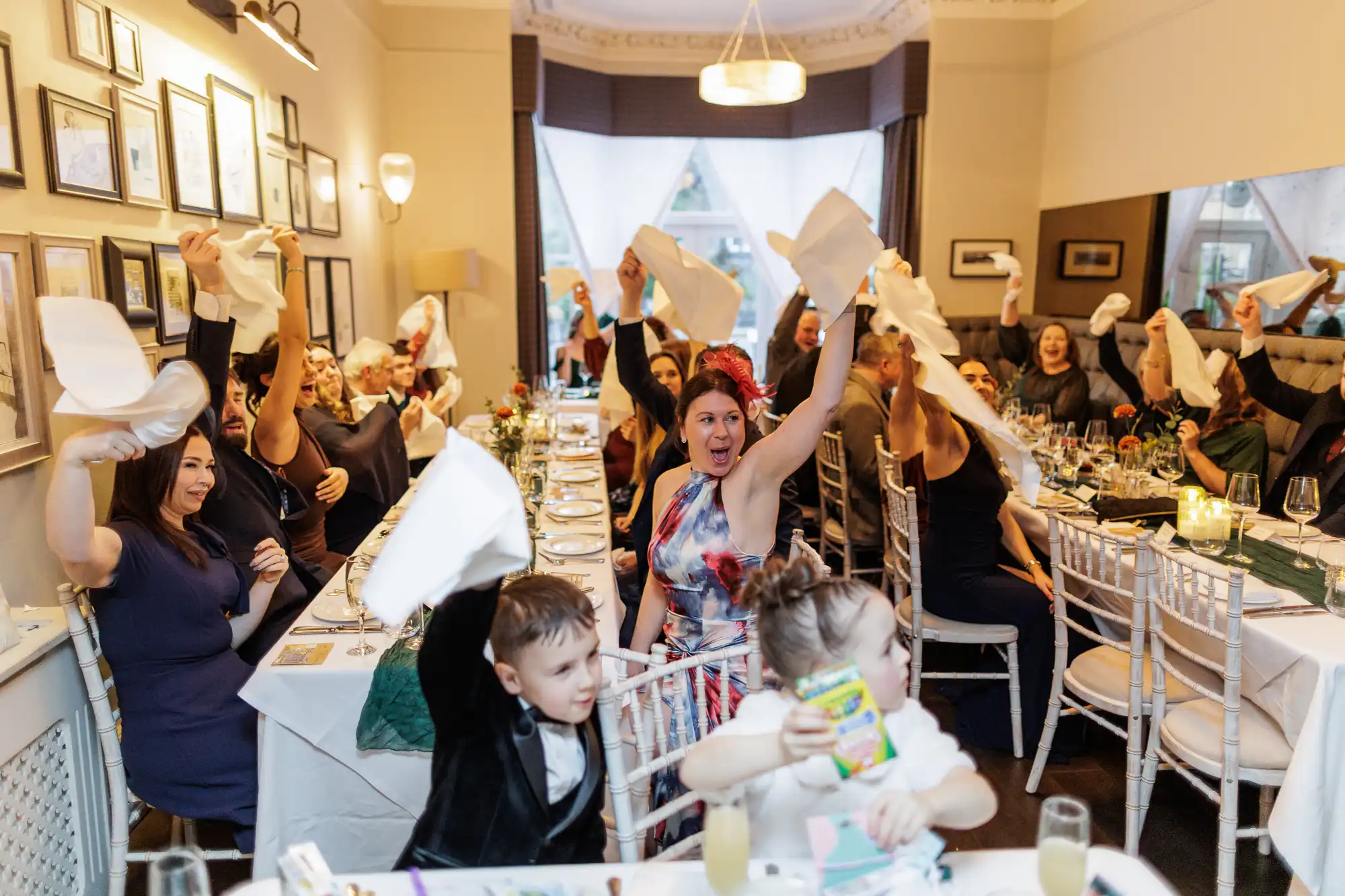 A lively celebration at a formal dinner with guests joyfully waving white napkins in the air, raising them above their heads in unison.