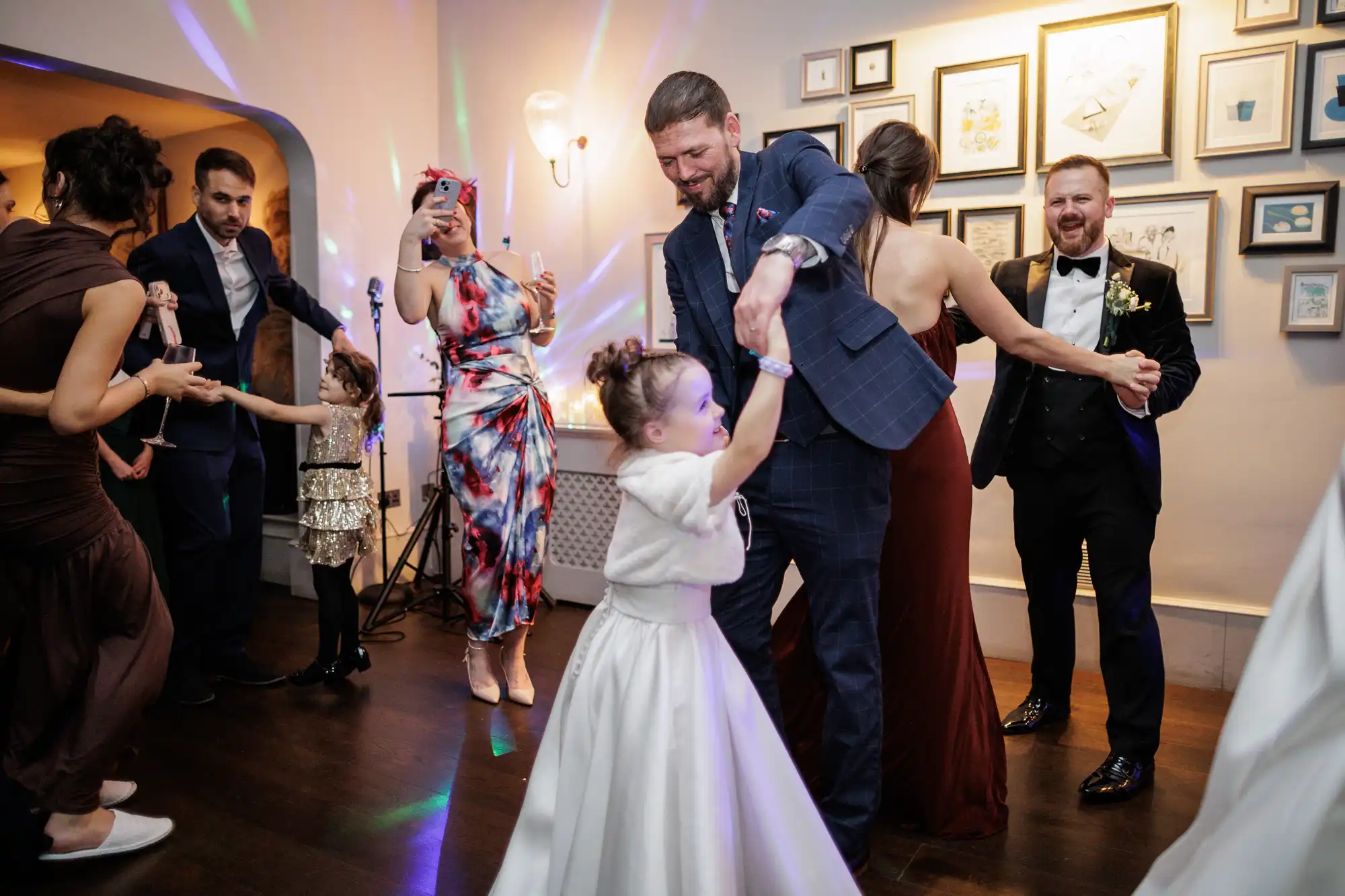 A bride, groom, and wedding guests dance at a reception. Colorful lights flash on the dance floor.