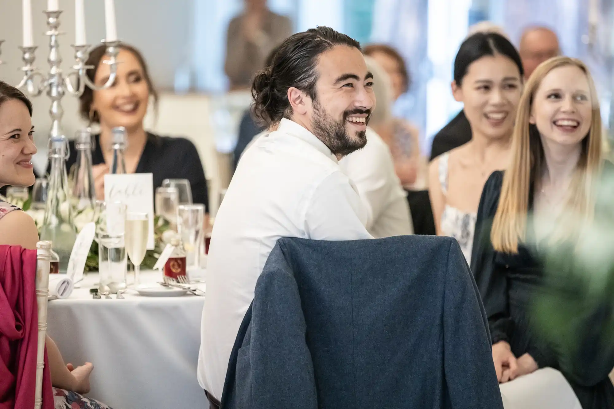 A group of people sitting around a table at a formal event, smiling and engaged in conversation. Candles and drinks are on the table.