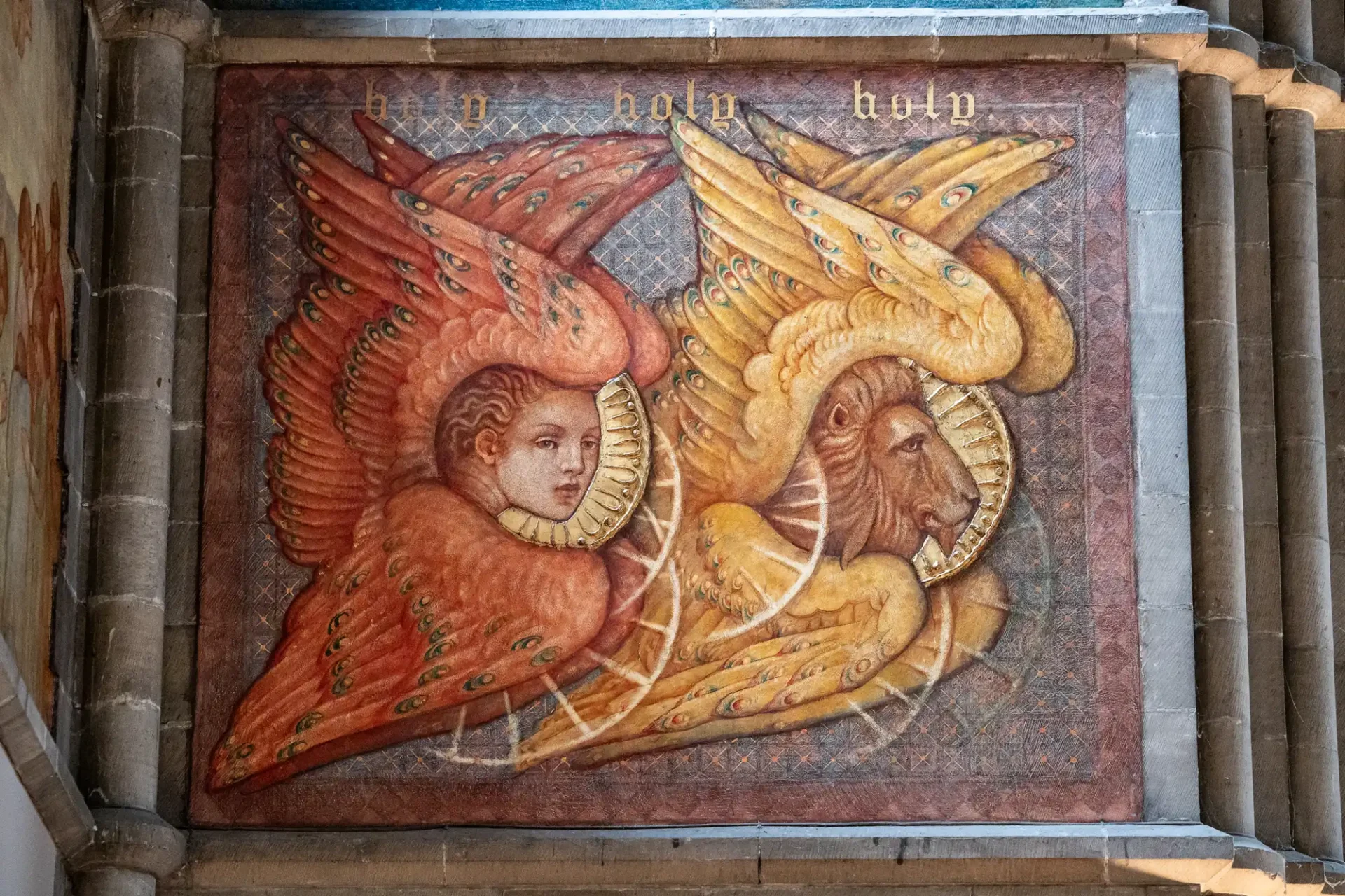 Mural painting with a human head and a lion head, both with wings and haloes, on a wall. The words "holy holy holy" are above them.